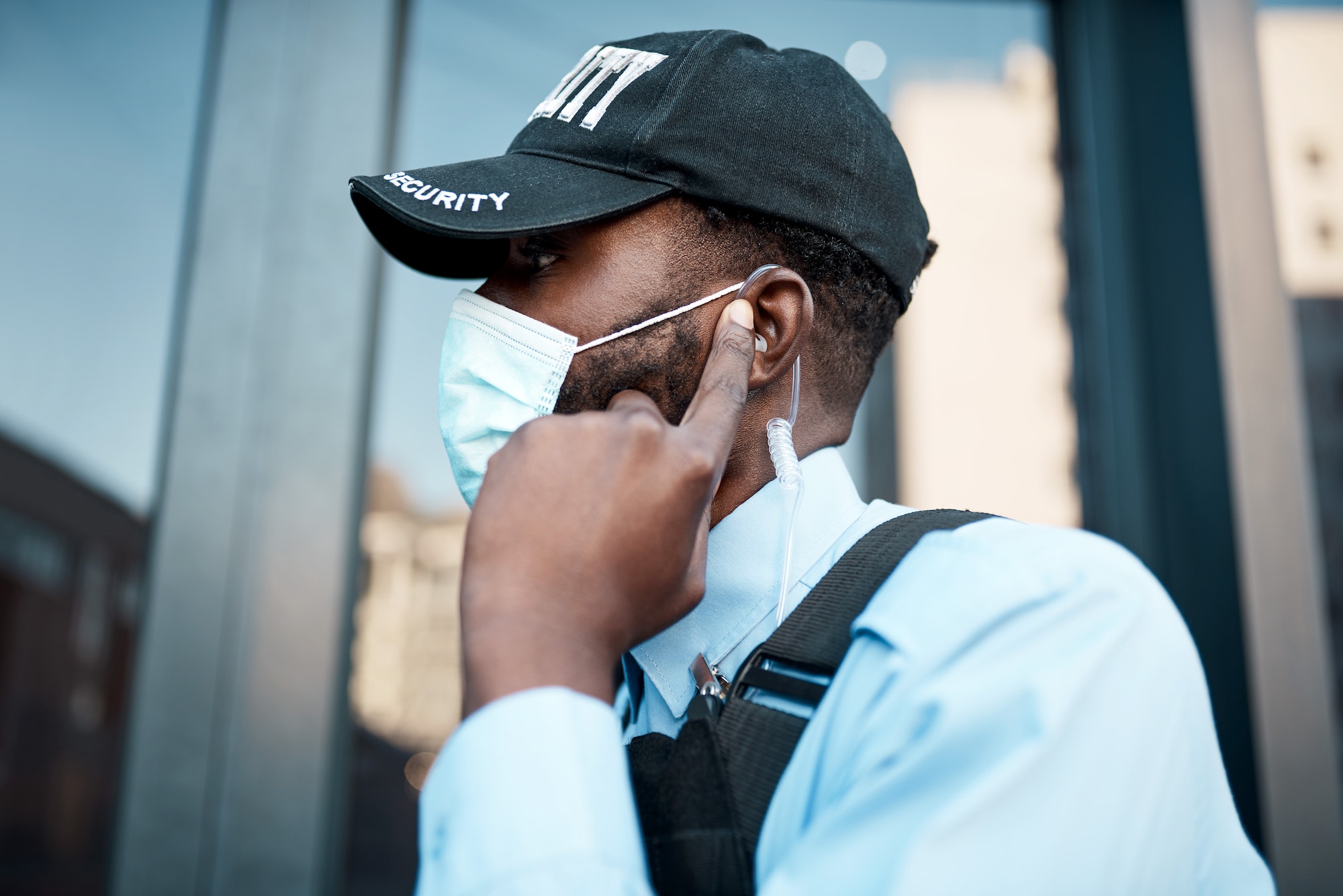 Shot of a masked young security guard using an earpiece while on patrol outdoors